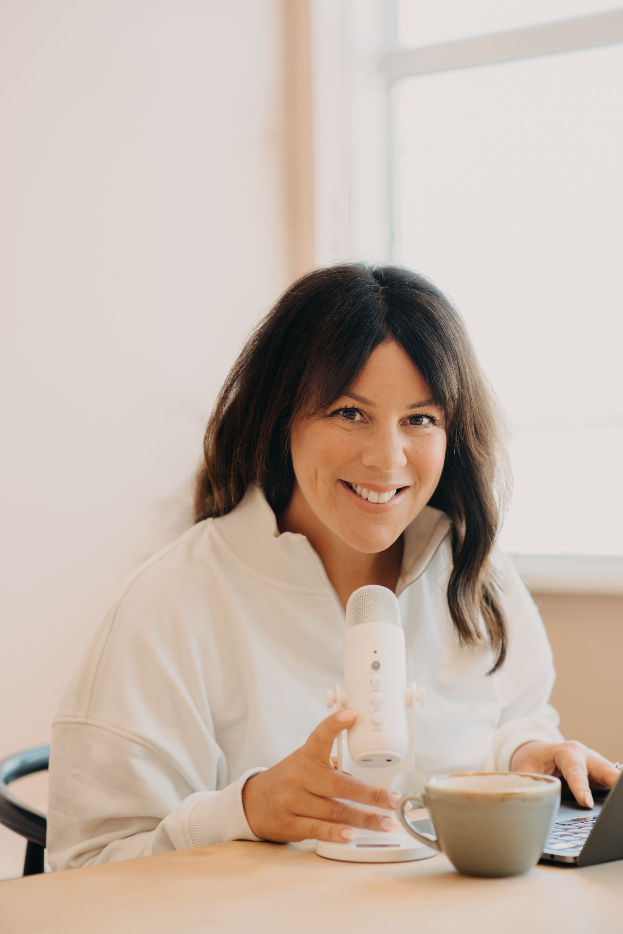 Jenna smiling at her desk with a coffee and microphone